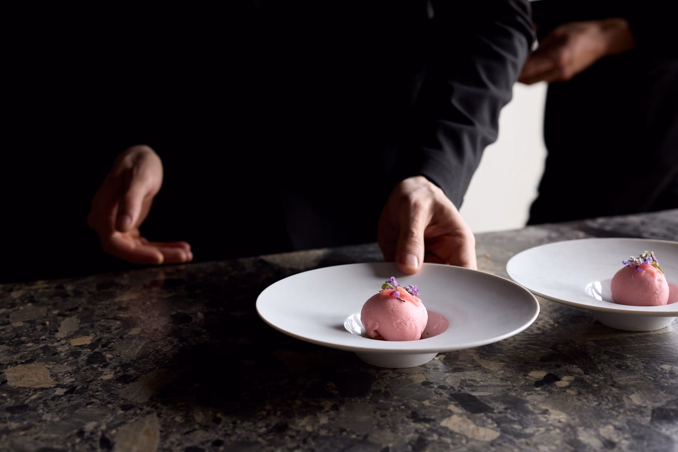 Chef plating pink sorbet scoops topped with purple flowers