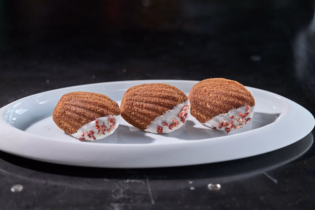 Three madeleines dipped in white chocolate and crushed freeze-dried berries