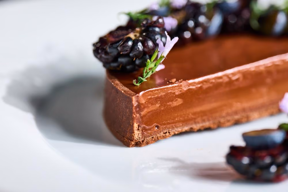 Chocolate tart garnished with blackberries and purple flowers
