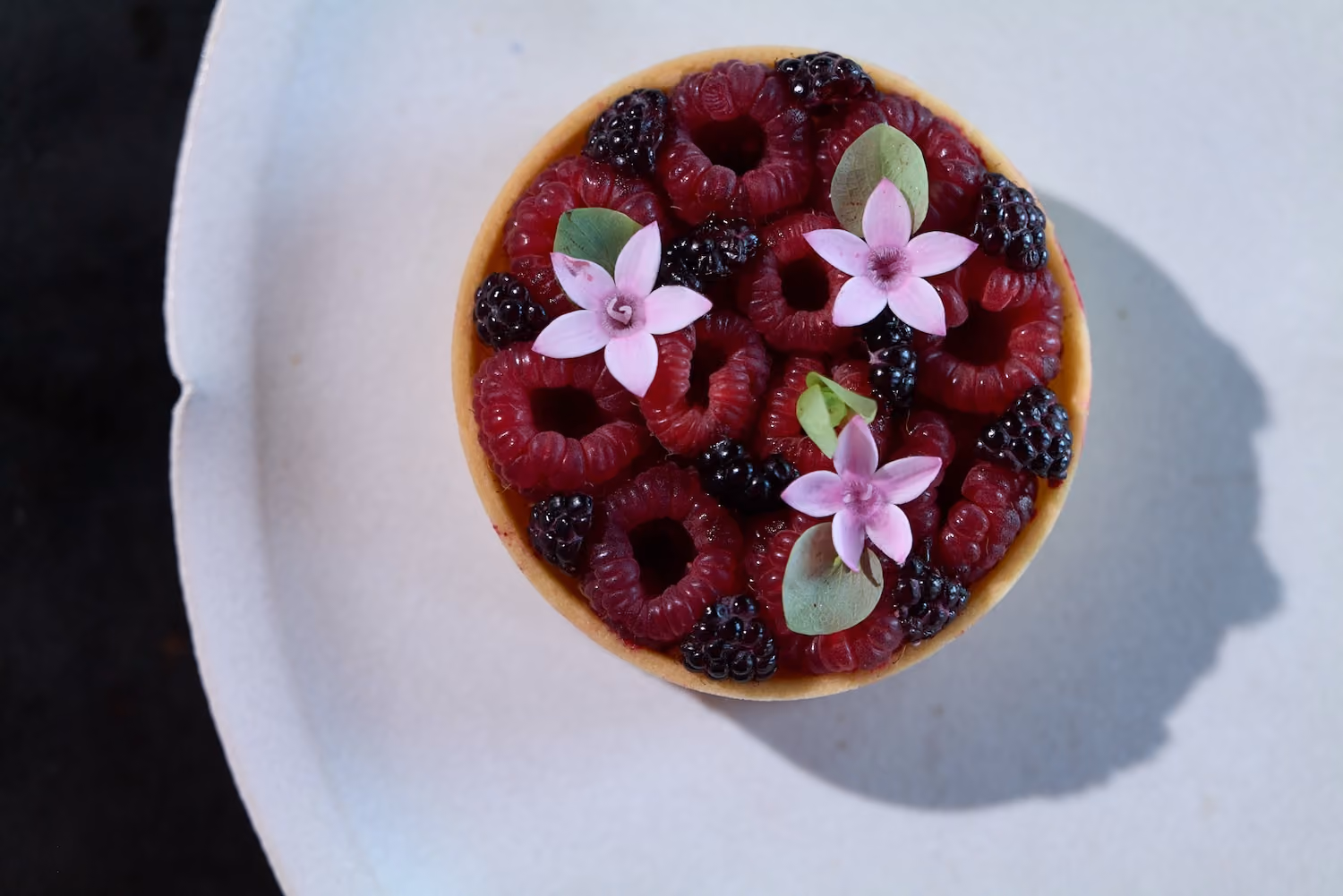 Overhead tart topped with raspberries, blackberries, and pink flowers