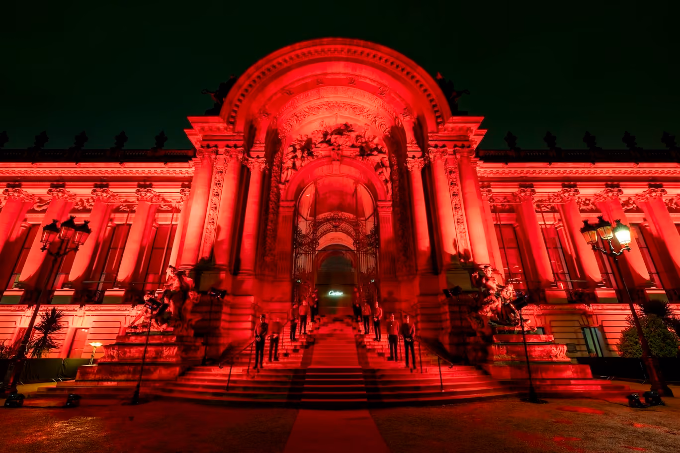 Red-lit grand building facade at night with event guests on the entrance stairs