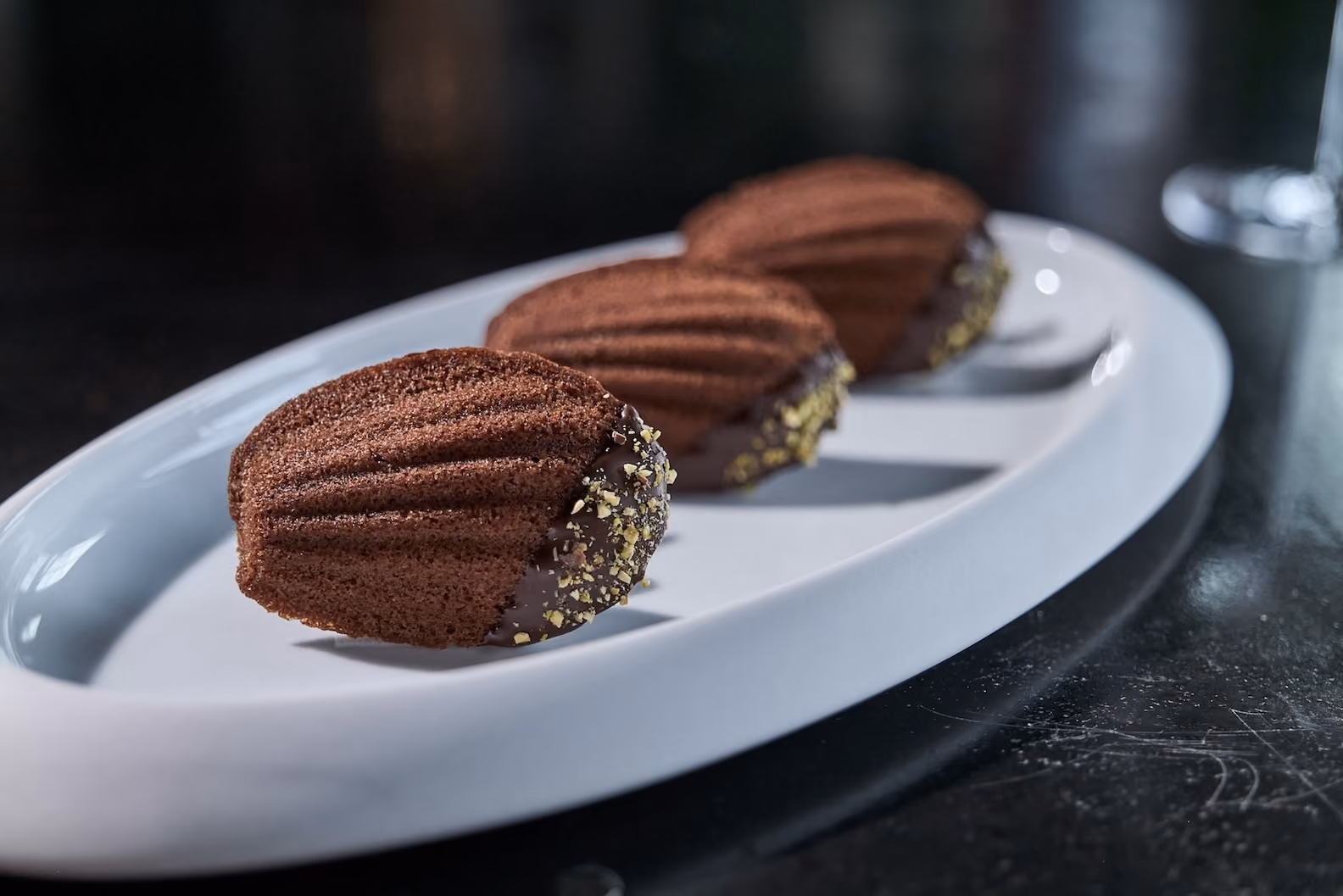 Three chocolate-dipped madeleines coated with crushed pistachios