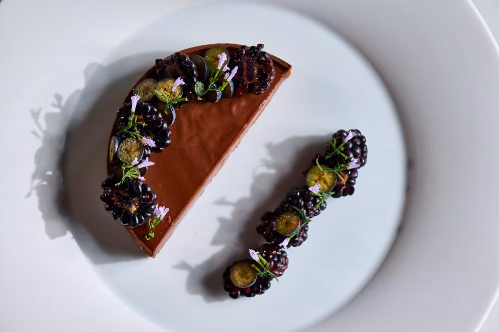 Chocolate tart garnished with blackberries, grapes, and purple flowers, with a matching berry garnish beside it