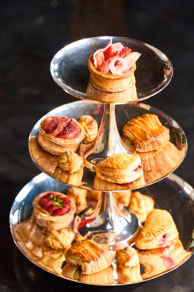Three-tiered stand of pastry canapés topped with fruit and shaved ham