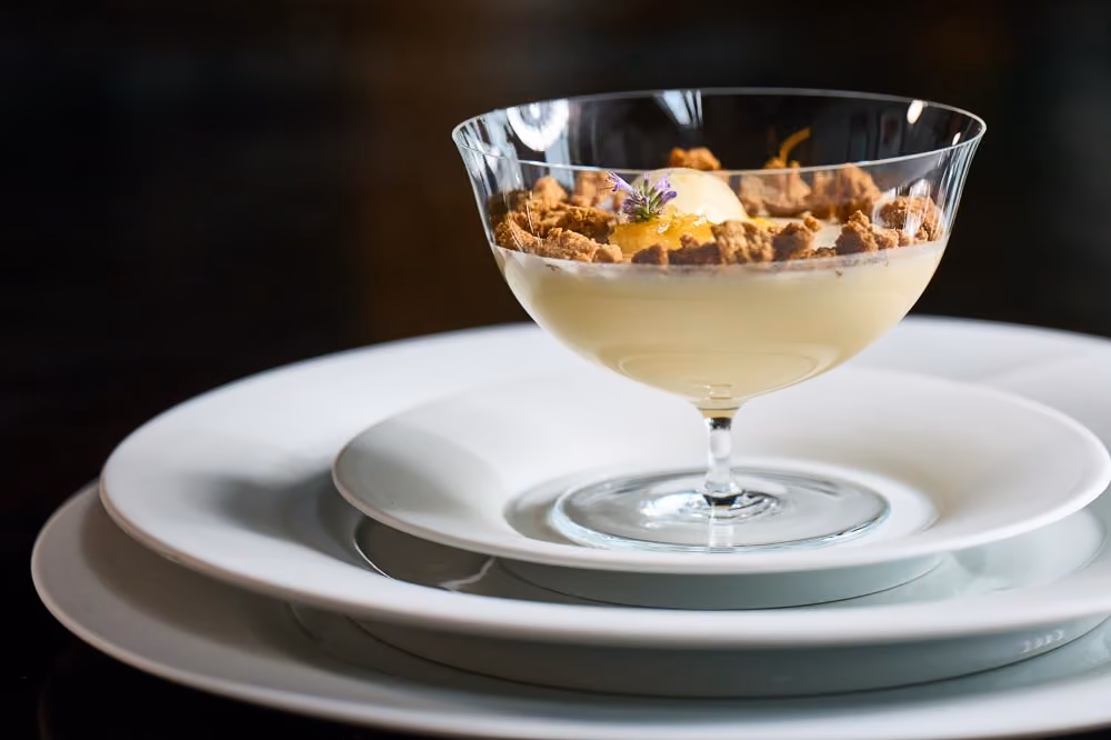 Layered dessert in a coupe glass with cream, crumble, and a lavender sprig