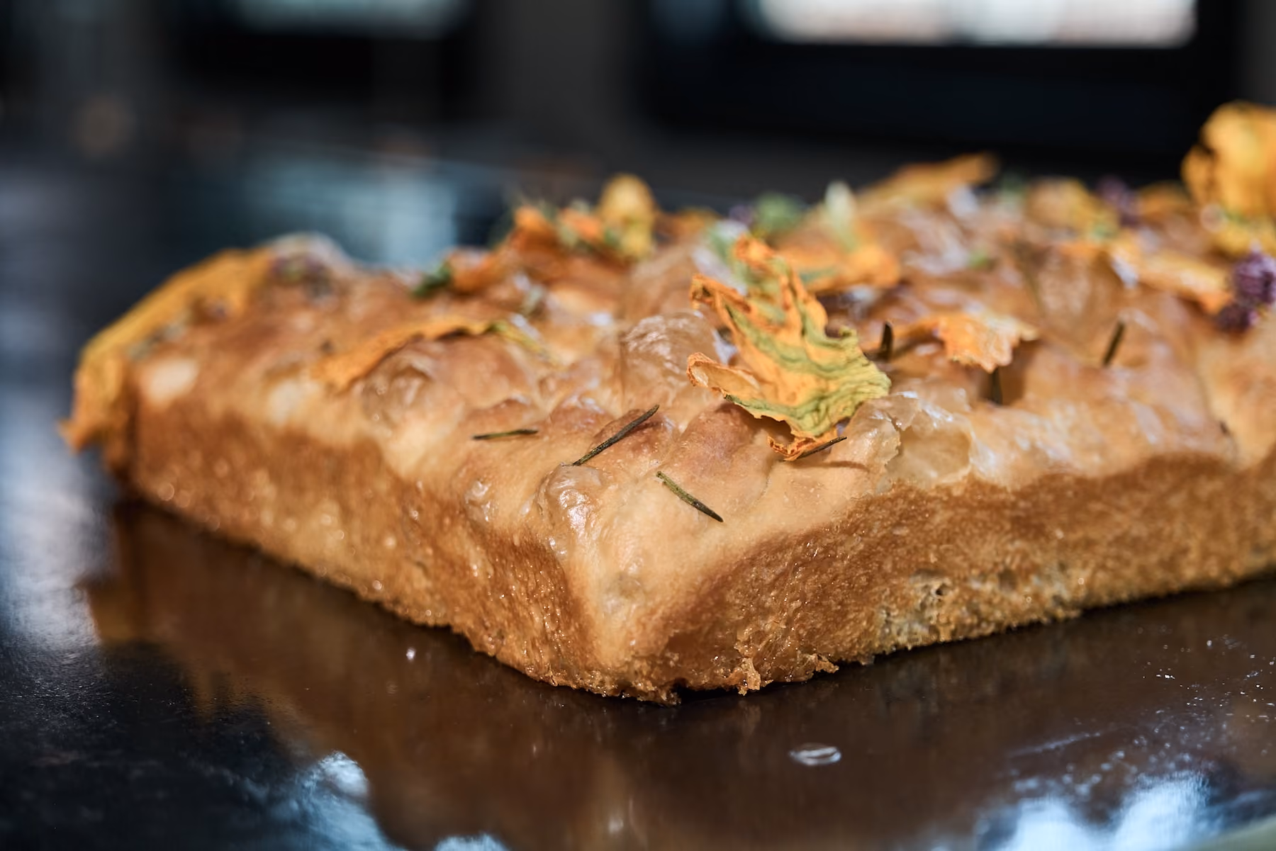 Close-up of focaccia bread topped with squash blossoms and rosemary