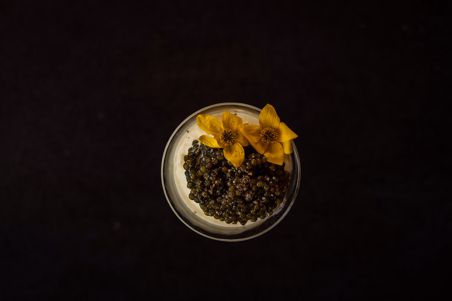 Overhead bowl of caviar topped with yellow flowers