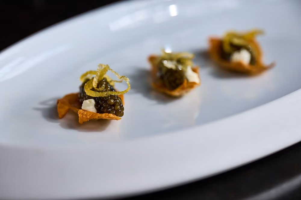 Three crispy tuile canapés topped with caviar, crème fraîche, and citrus zest