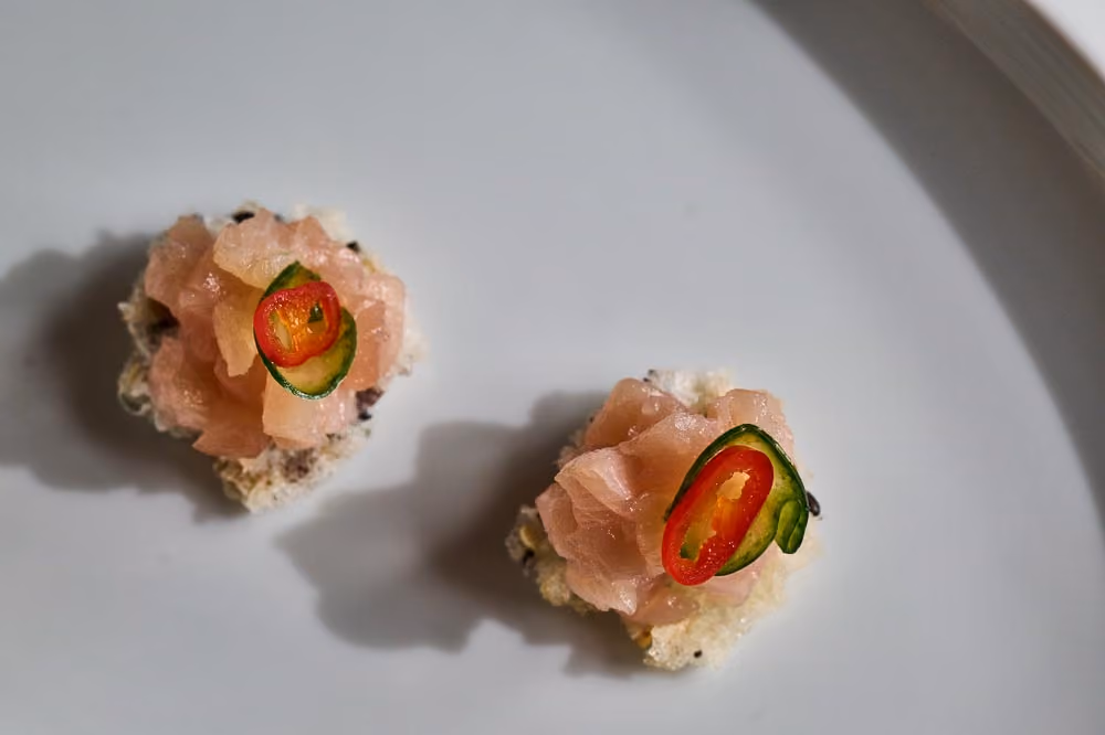 Two crispy rice cracker canapés topped with diced tuna, cucumber, and chili