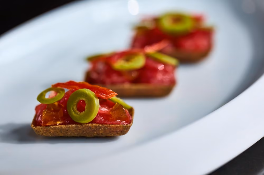 Three crispy crackers topped with tomato tartare and pickled green chili slices