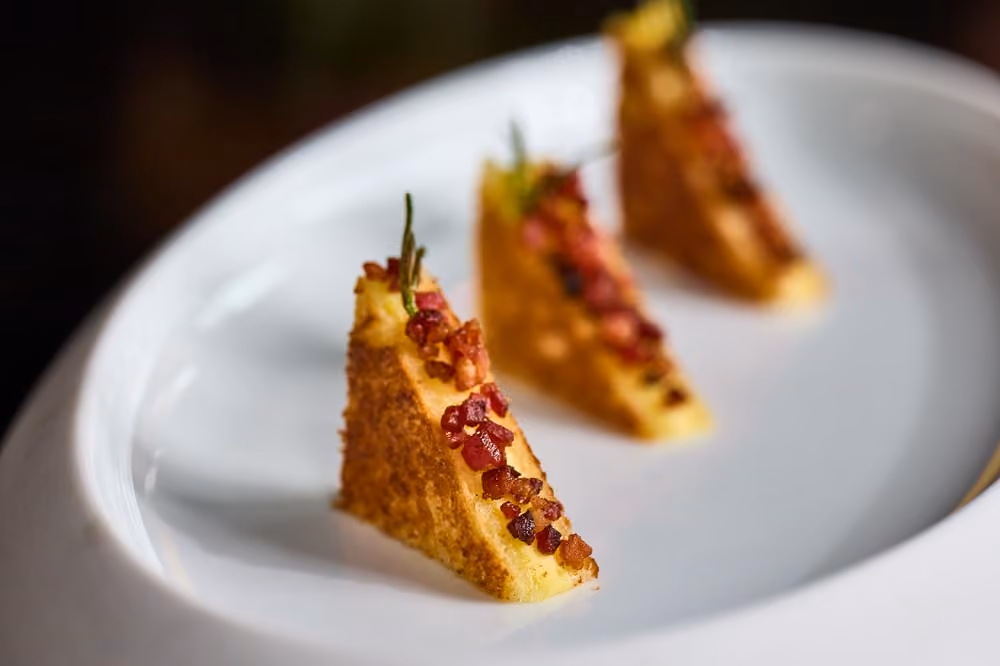 Three cornbread wedges topped with diced ham and rosemary