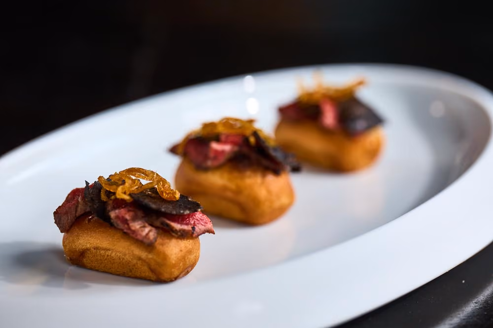 Three brioche bites topped with sliced steak, black truffle, and crispy fried shallots