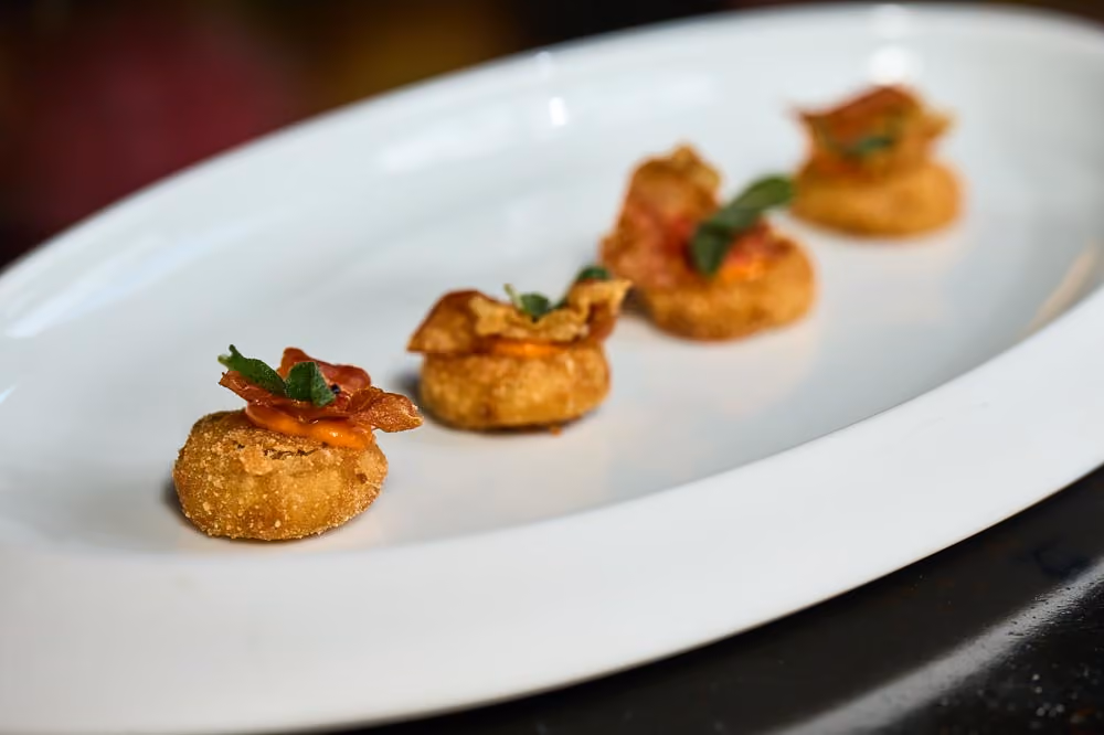 Four fried croquette bites topped with prosciutto and herbs