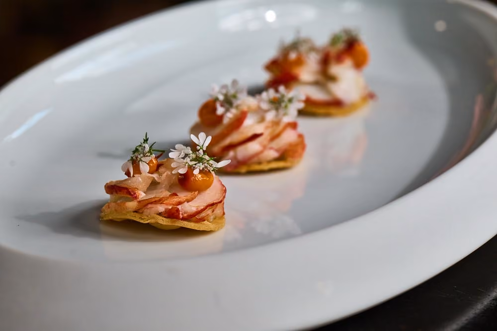 Crispy tostada canapés topped with sliced ham and white flowers