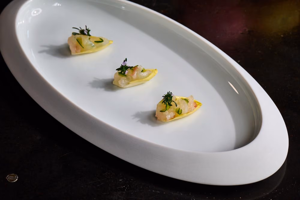 Three yellow endive leaf canapés topped with diced fish and herbs