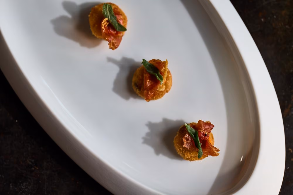 Three crispy croquette bites topped with prosciutto and fried sage