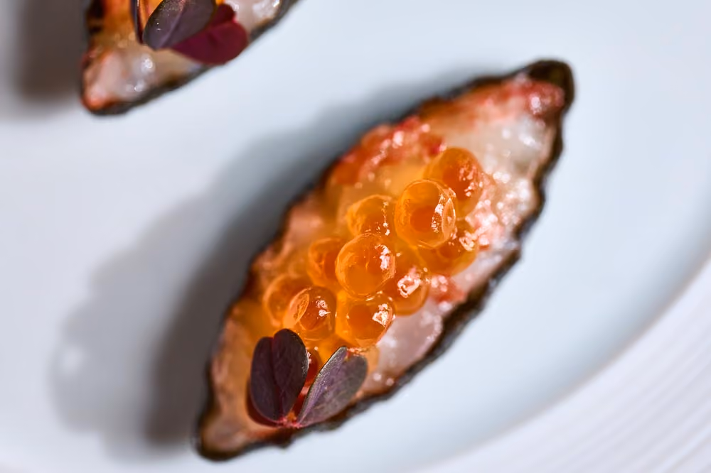 Fish crudo bite topped with orange roe and purple microgreens