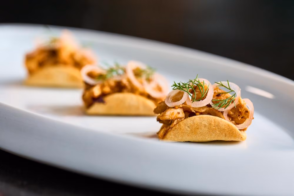 Three taco-shaped canapés topped with shredded chicken and pickled shallot rings, garnished with dill