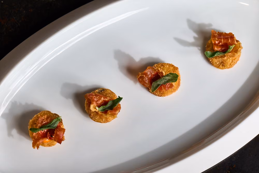 Four crispy potato rounds topped with tomato, prosciutto, and fried sage