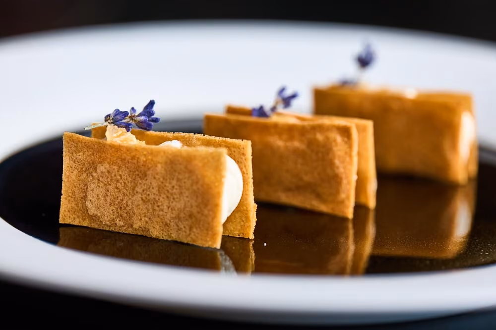 Three crepe pastry canapés filled with cream and topped with lavender sprigs