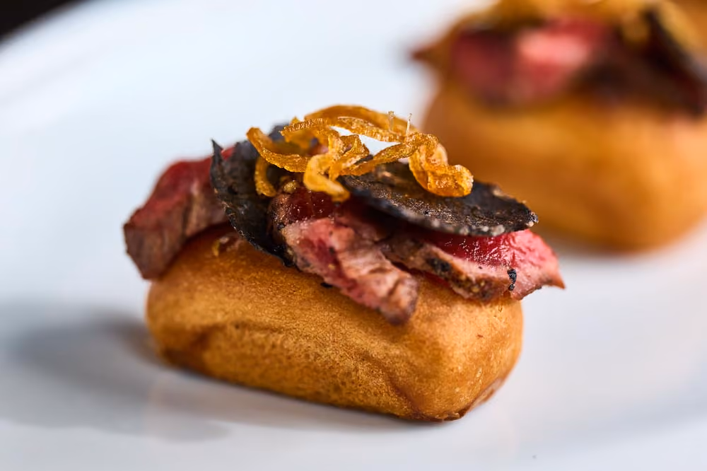 Brioche bite topped with sliced steak, black truffle, and crispy fried shallots
