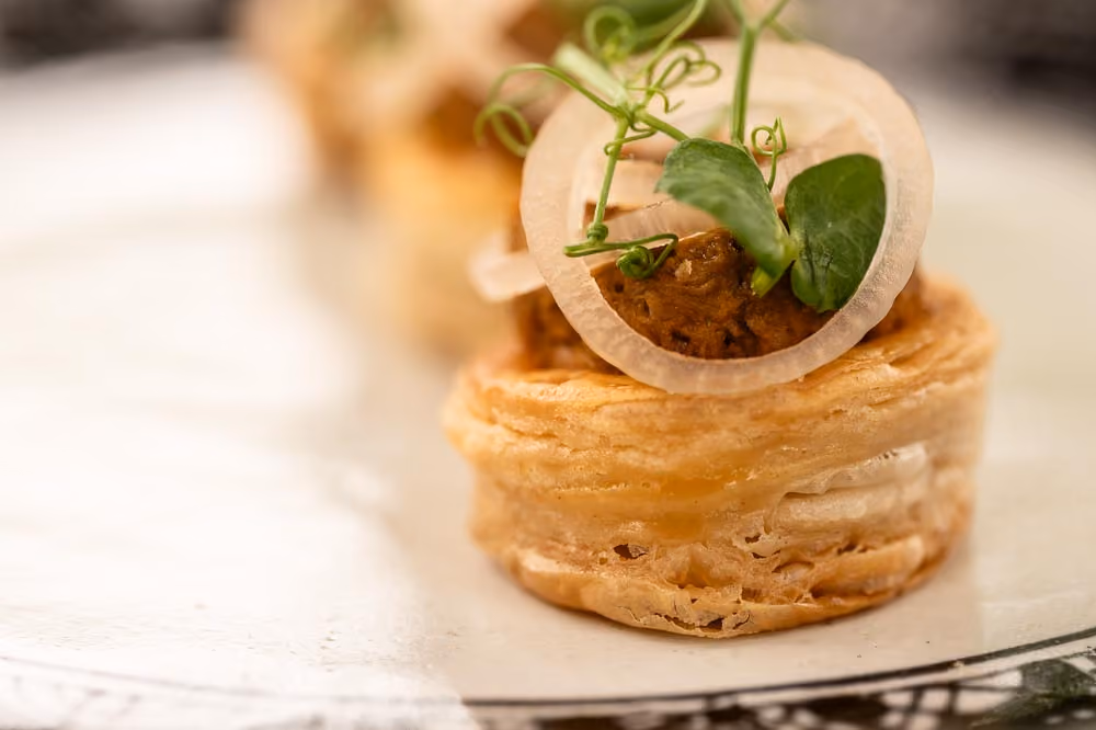 Vol-au-vent pastry canapé topped with braised meat, pickled onion, and pea shoots