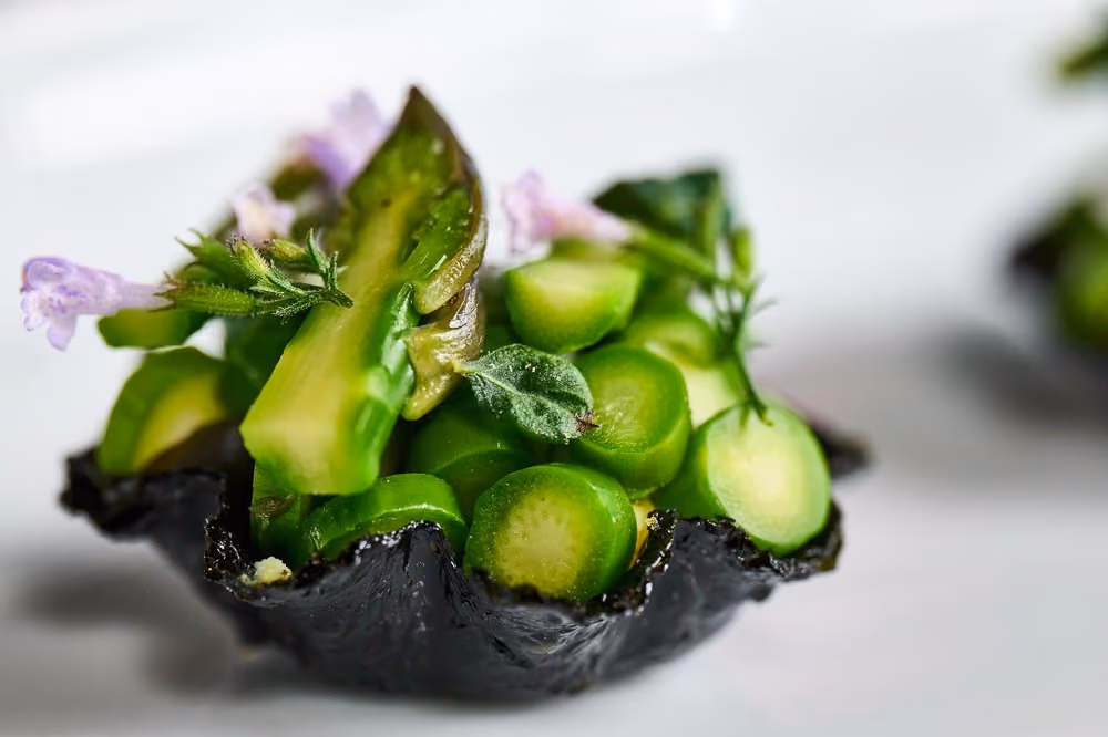 Black tart shell filled with sliced asparagus, radish, and purple flowers