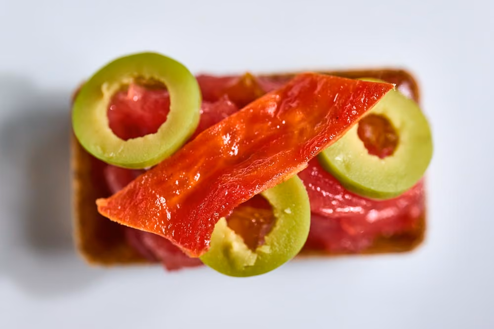 Crispy cracker topped with tomato tartare, avocado rounds, and a dried tomato crisp