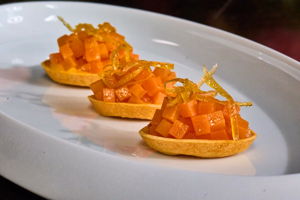 Three tartlet shells filled with diced papaya and topped with candied citrus zest