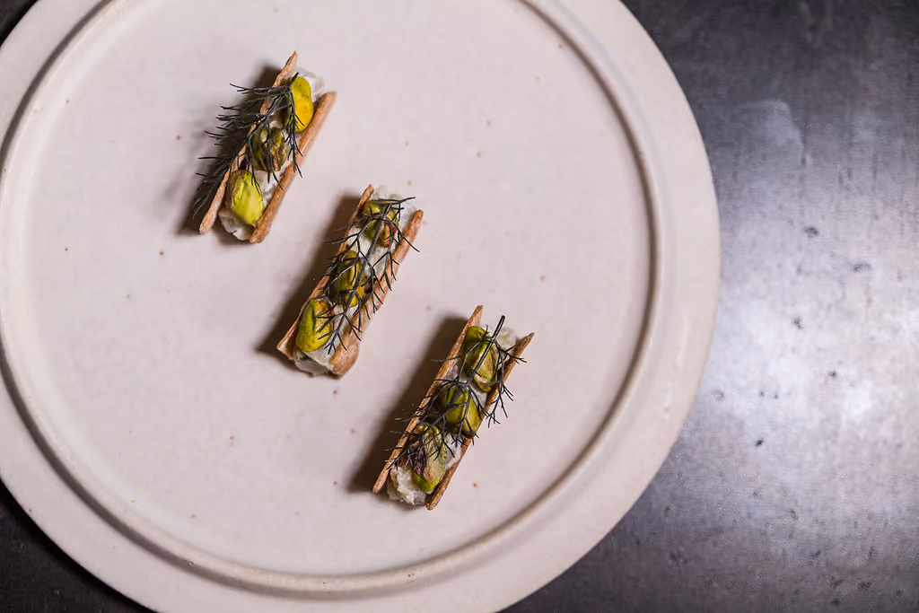 Crostini topped with burrata and pistachios, three pieces on a round plate