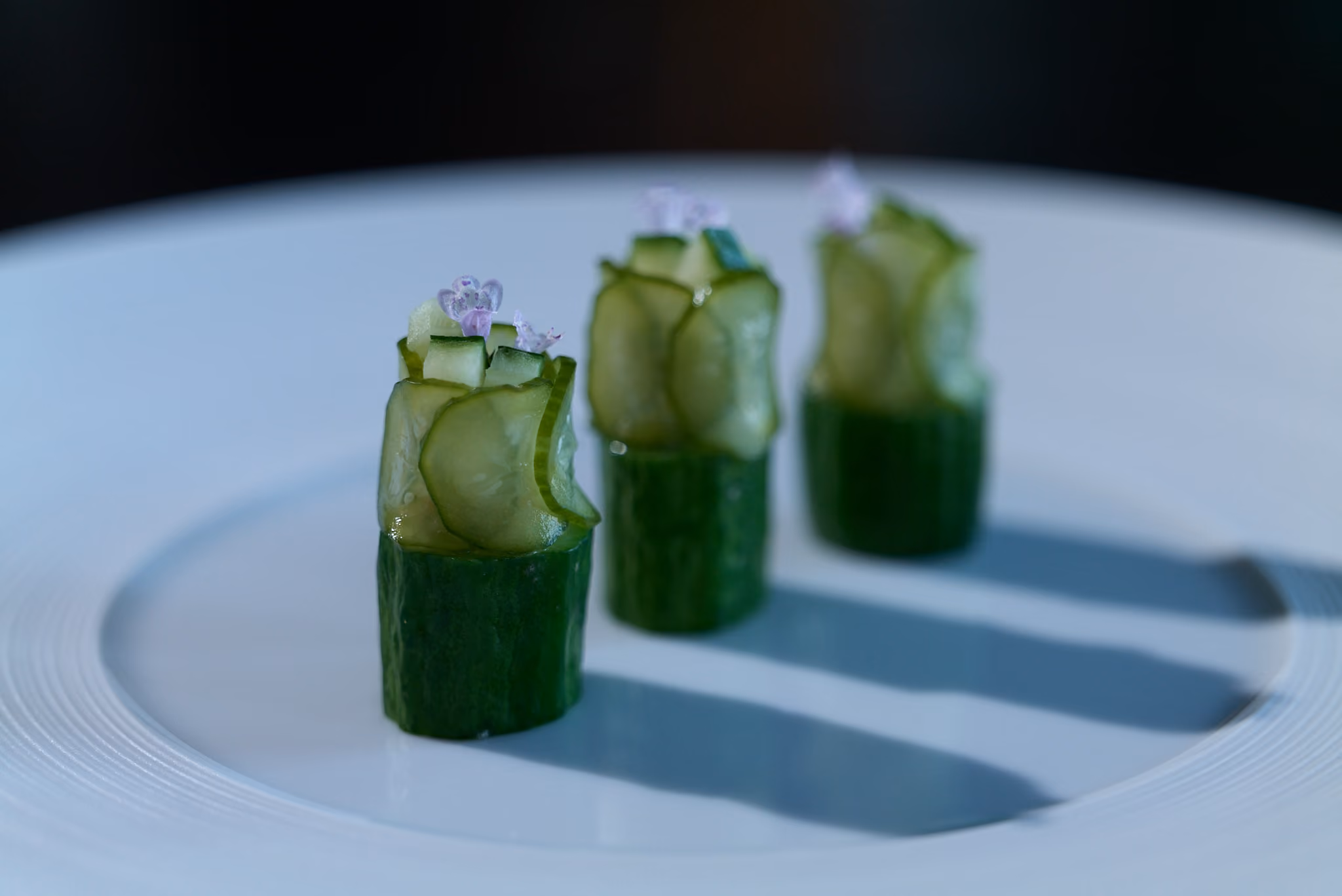Three cucumber roll canapés topped with purple flowers