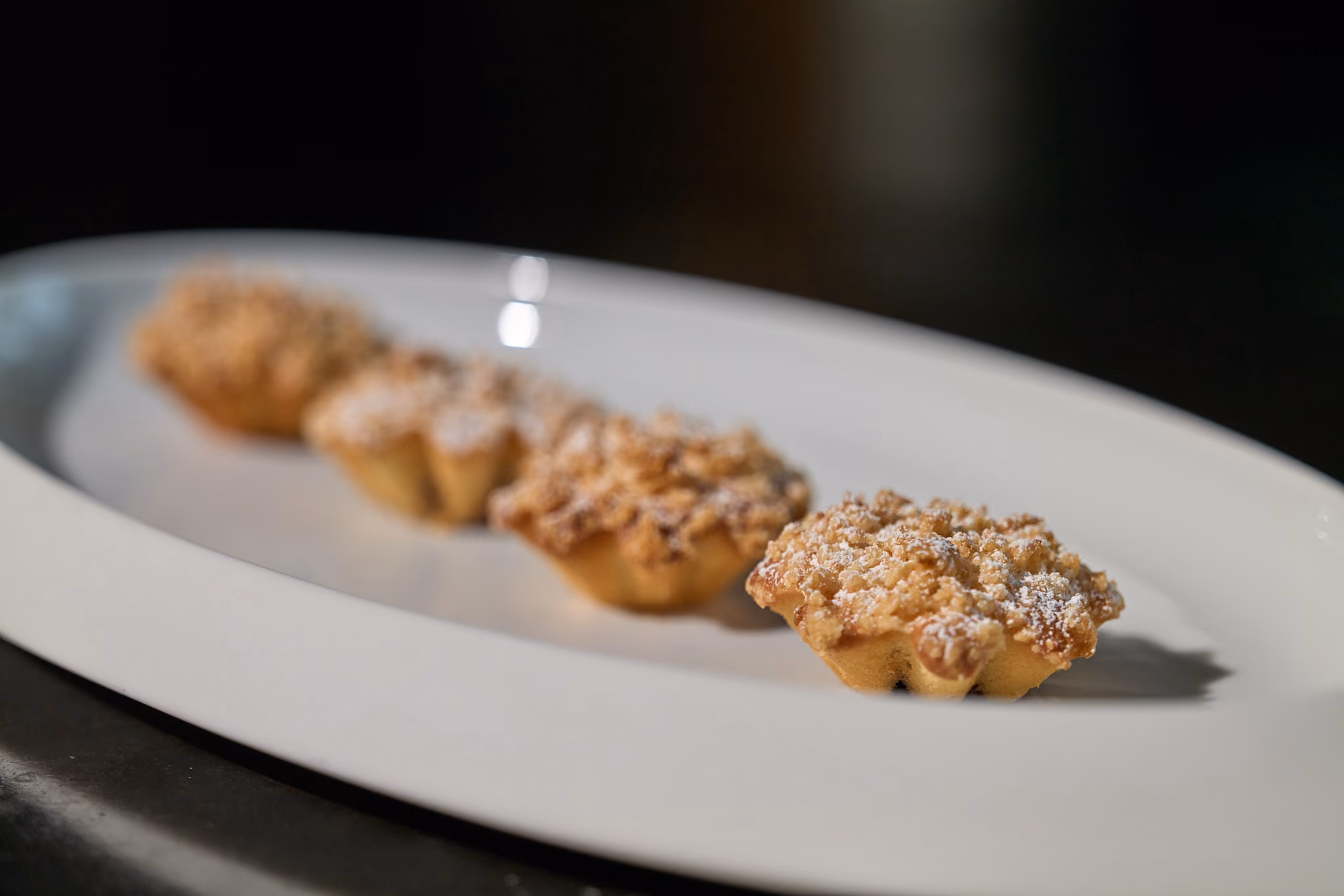 Four crumble-topped mini tarts dusted with powdered sugar