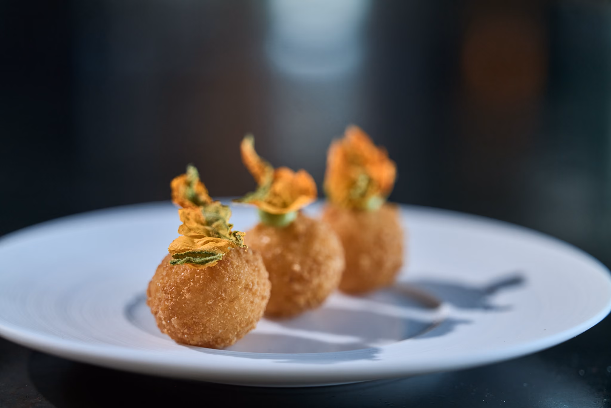 Three fried croquette bites topped with crispy squash blossom