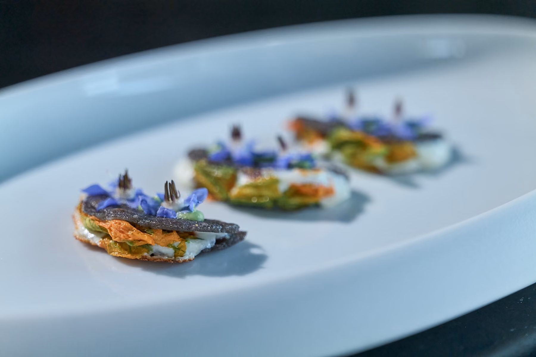 Black tuile canapés topped with avocado, herb cream, and purple flowers