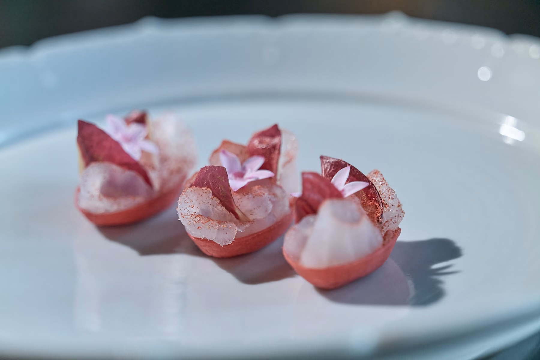 Row of pink canapé cups topped with seafood and purple flowers