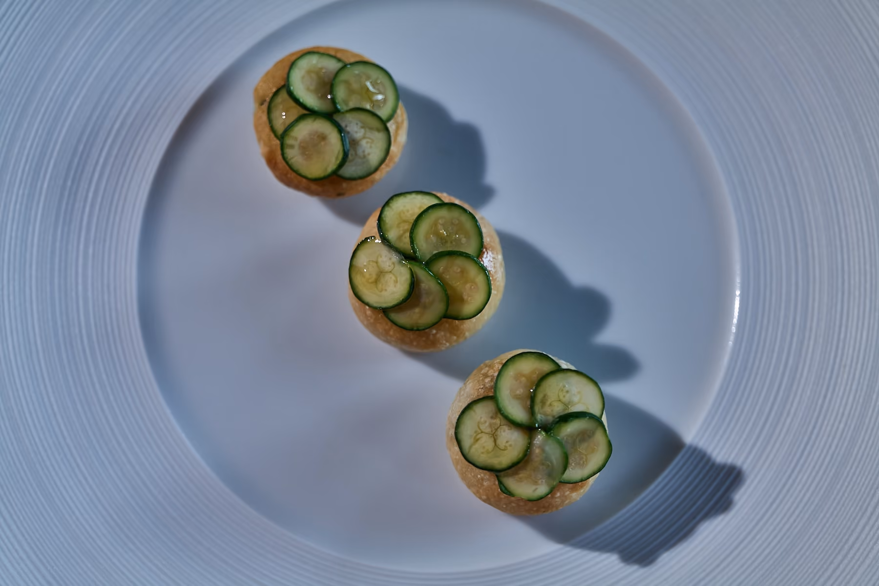 Overhead trio of brioche bites topped with overlapping cucumber slices