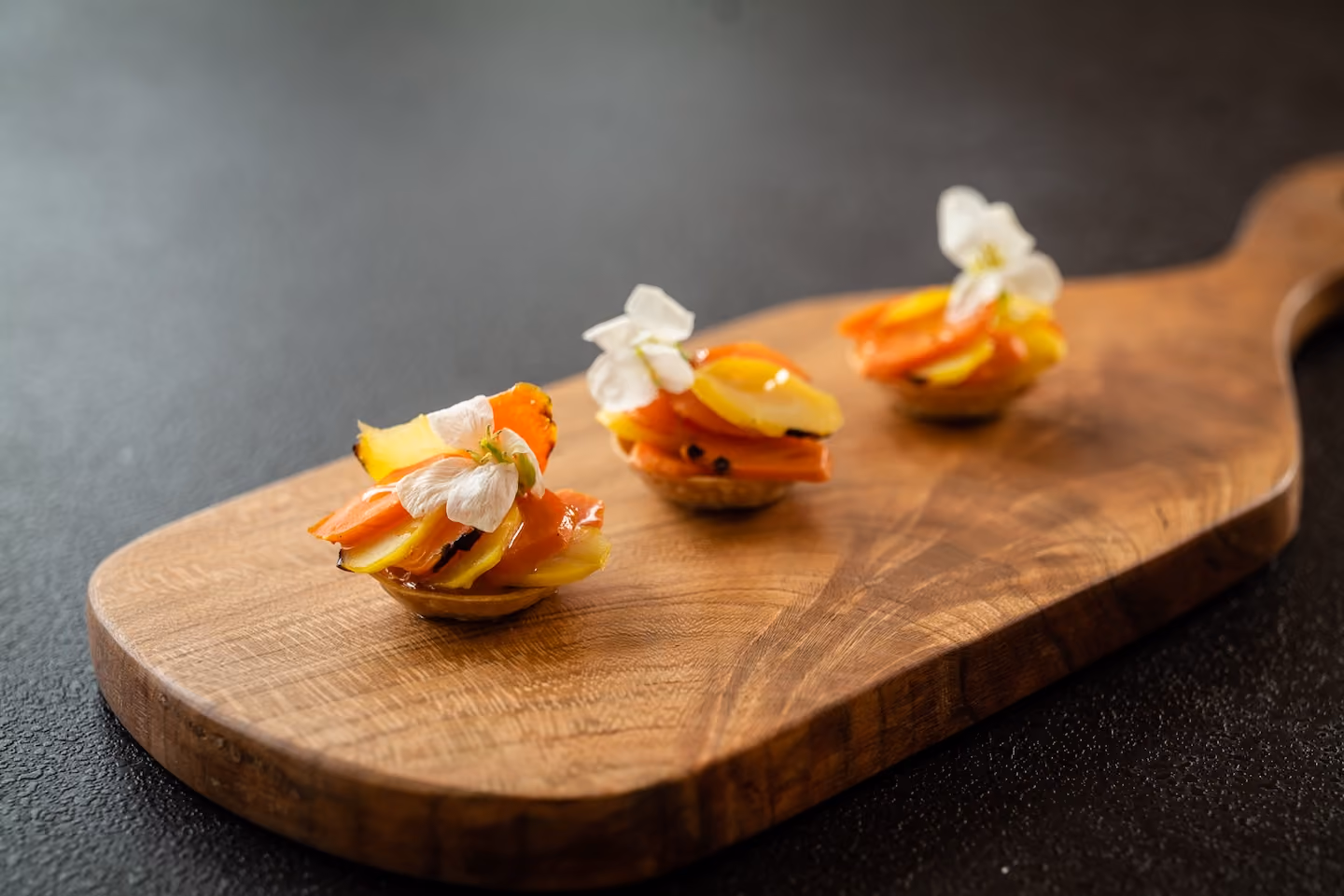 Row of tartlet canapés topped with grilled stone fruit and white flowers