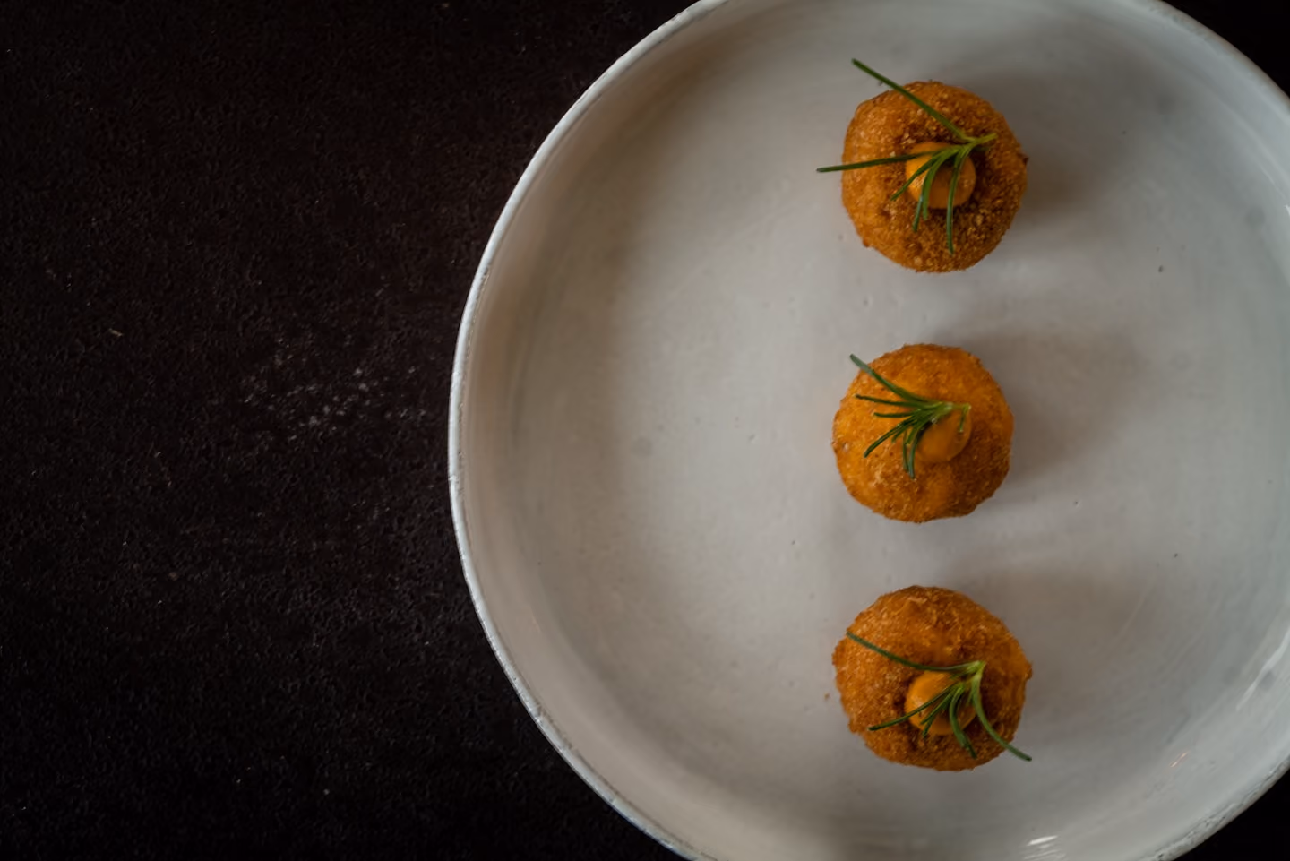 Overhead row of breaded croquettes topped with sauce and a rosemary sprig