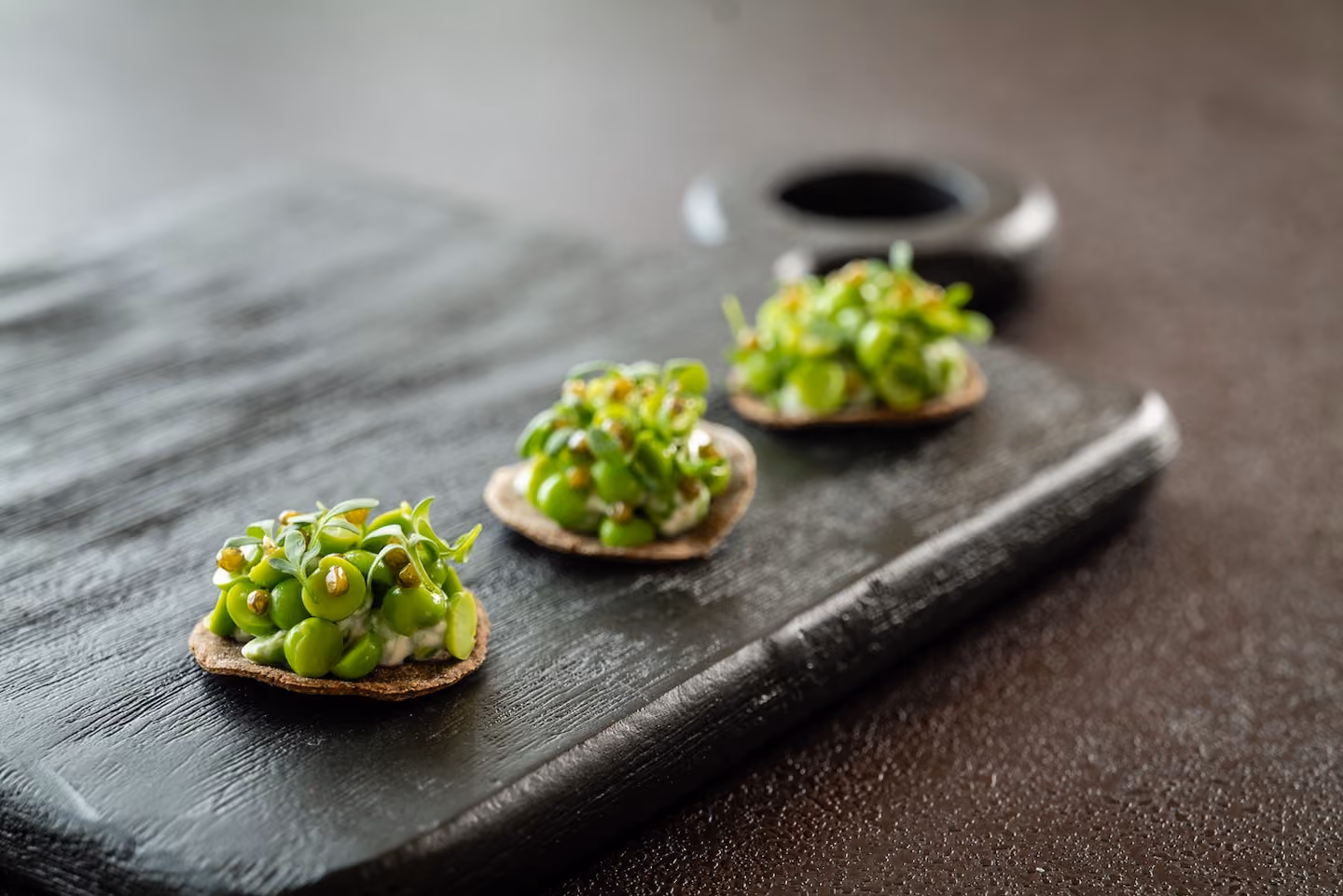 Row of crispy tuile canapés topped with peas, fava beans, and mustard seeds