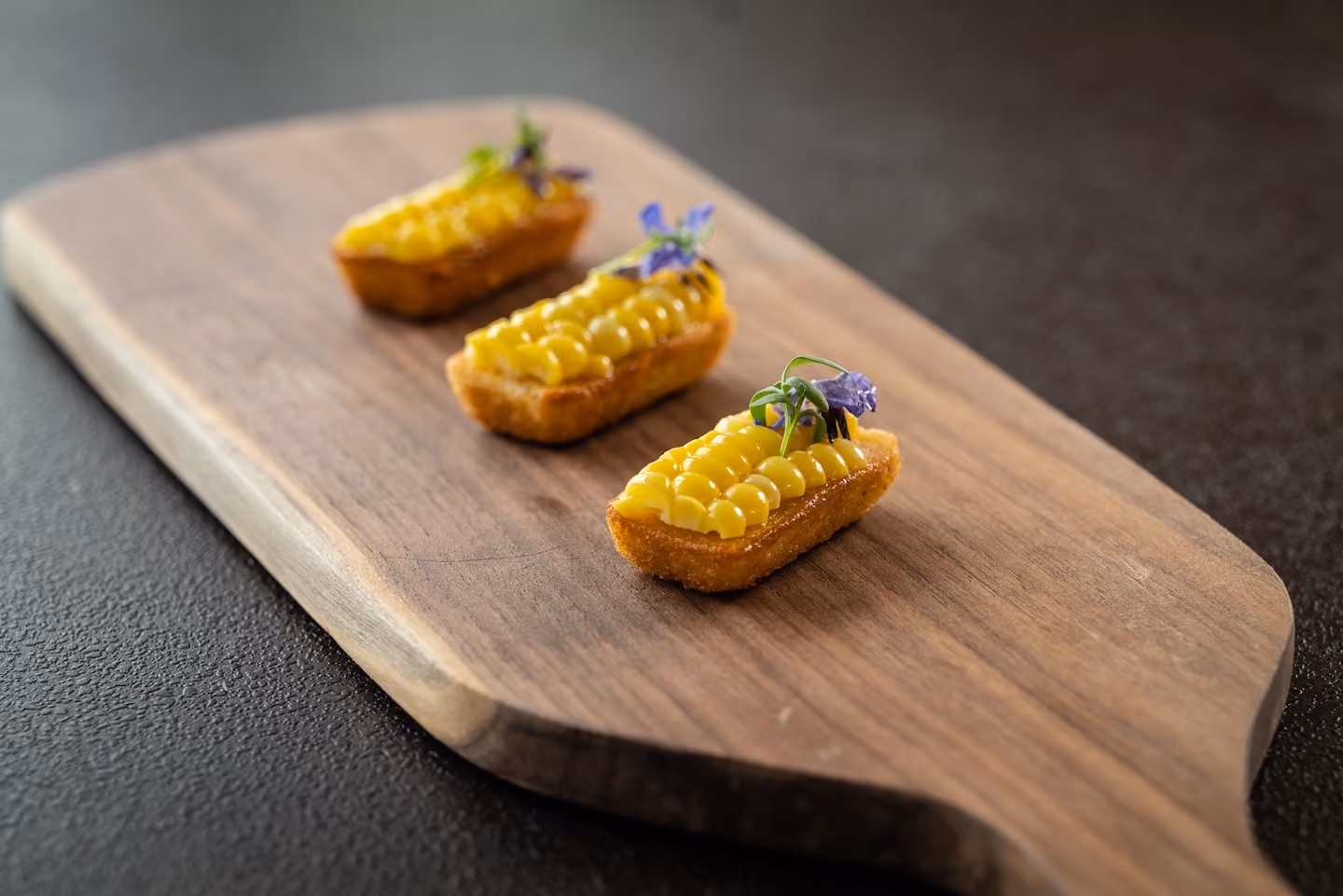 Row of corn-topped crostini garnished with purple flowers