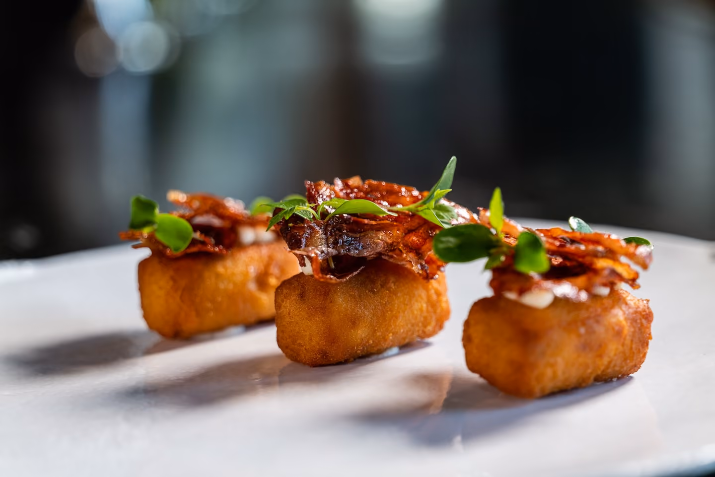 Row of fried croquette canapés topped with crispy prosciutto and herbs