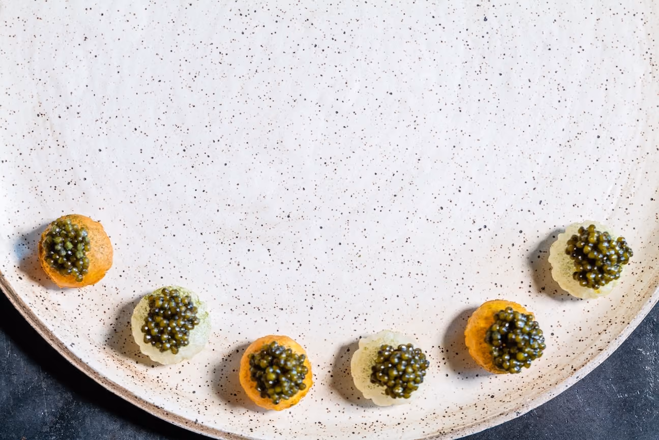 Assorted caviar canapés arranged in an arc on a speckled ceramic plate