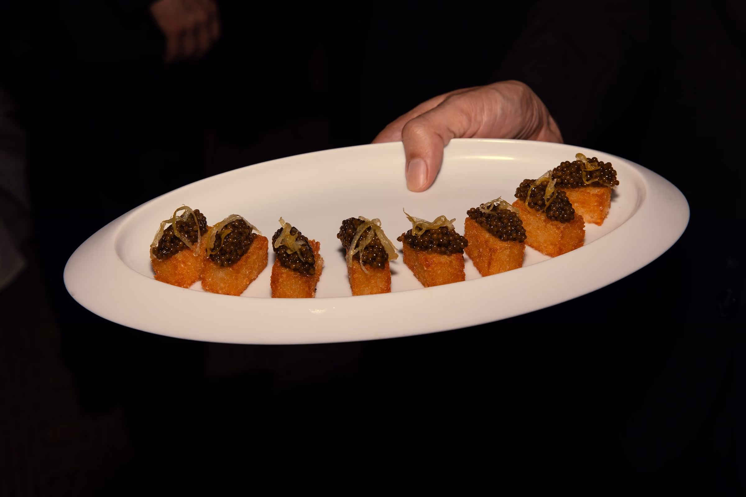 Row of crispy bite canapés topped with caviar held by a server