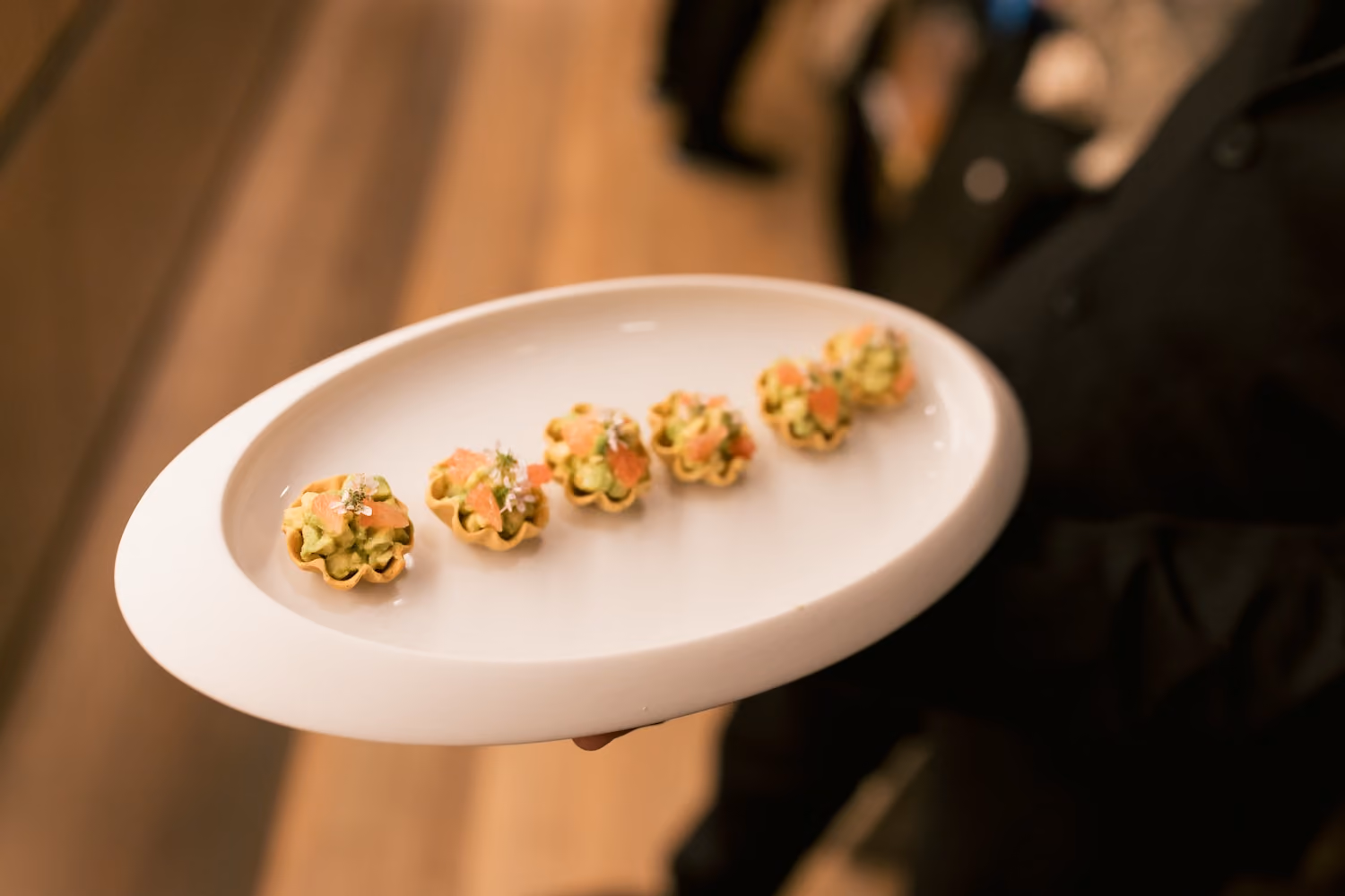 Tartlet canapés topped with avocado and salmon on a plate held by a server