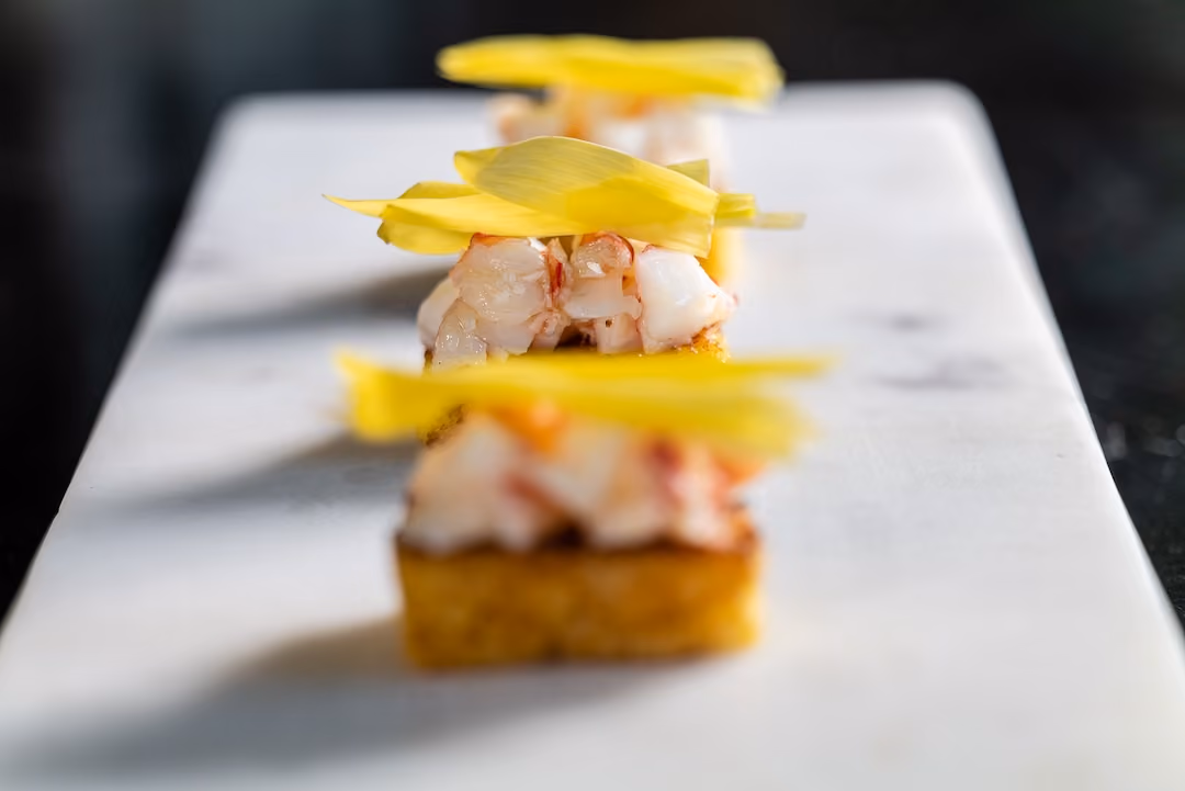 Row of crab canapés topped with thin yellow squash ribbons