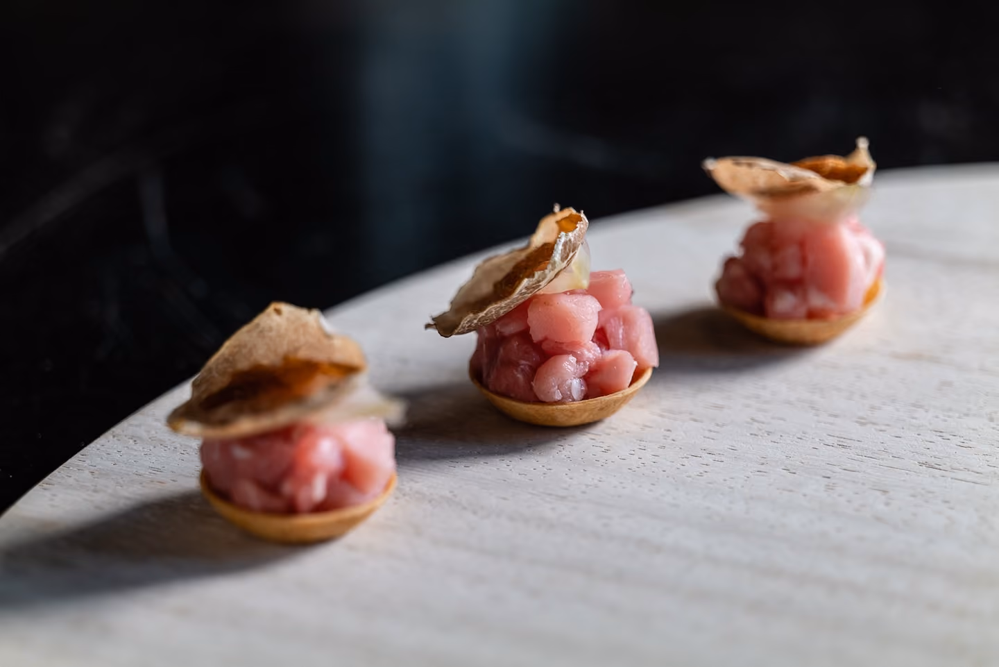 Row of tuna tartare canapés topped with crispy chips on a wooden board