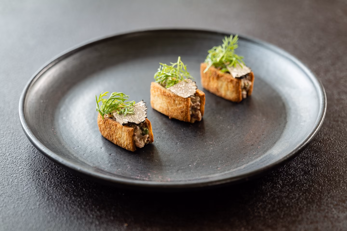 Three toasted canapés topped with mushroom filling, shaved truffle, and scallion
