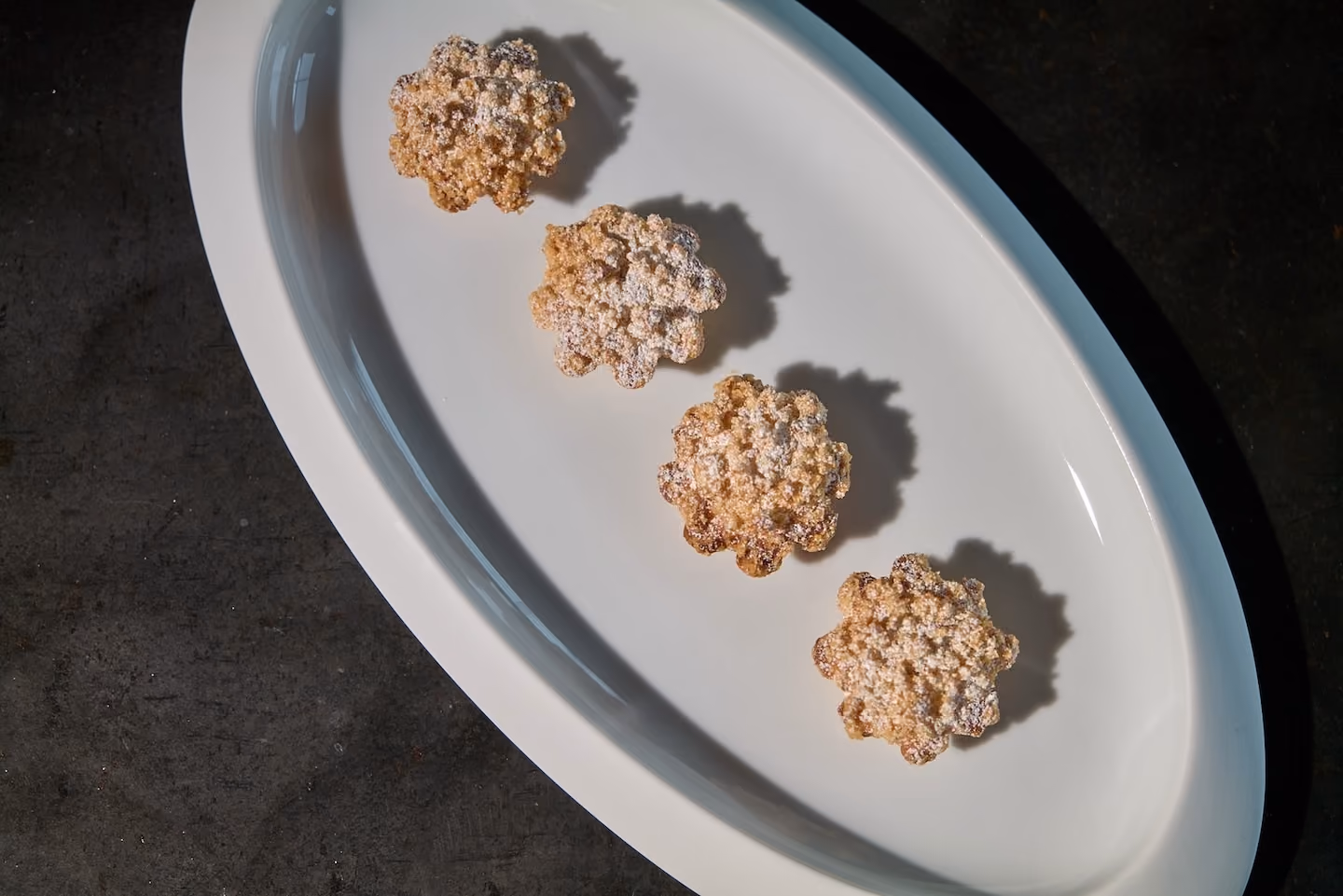 Four sugar-dusted almond florentine cookies on an oval white plate