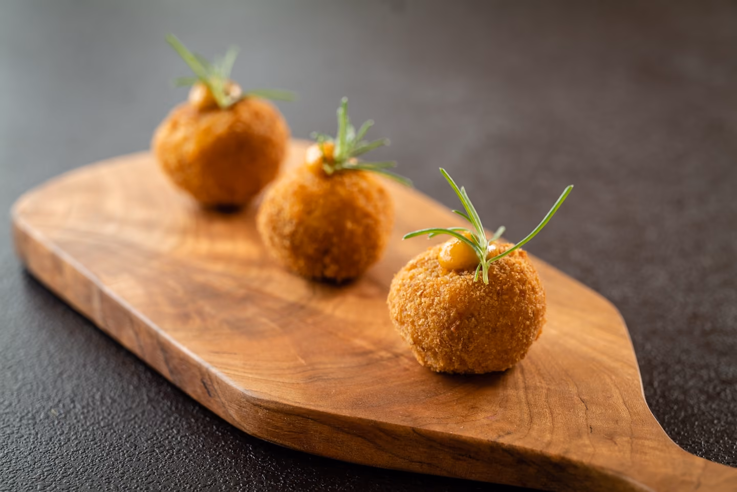 Row of breaded croquettes garnished with rosemary and a dollop of sauce