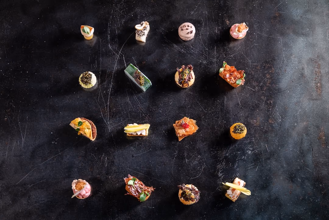 Overhead grid of assorted bite-sized canapés arranged on a dark surface
